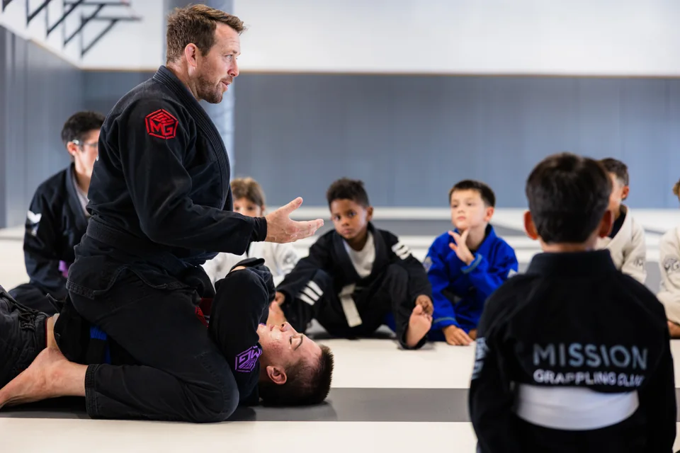 Adam Schmaltz demonstrates a technique while students watch on the mats