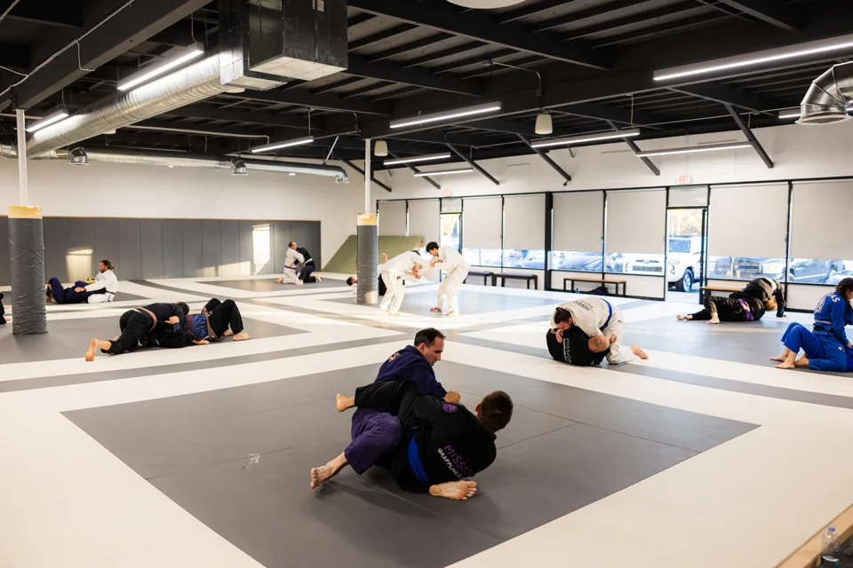 Pairs of students train across the bright Mission Grappling Club mat space